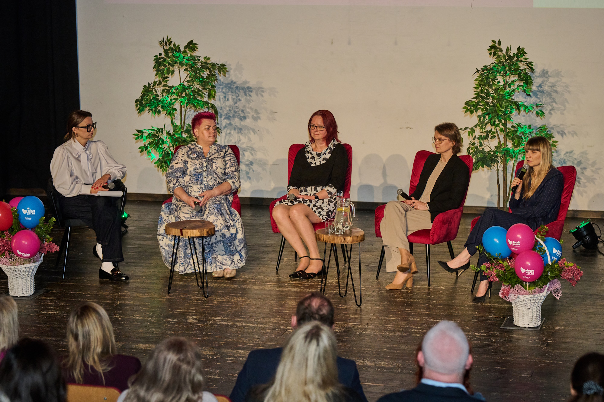 osoby na scenie siedzą na krzesłach - prelegenci konferencji