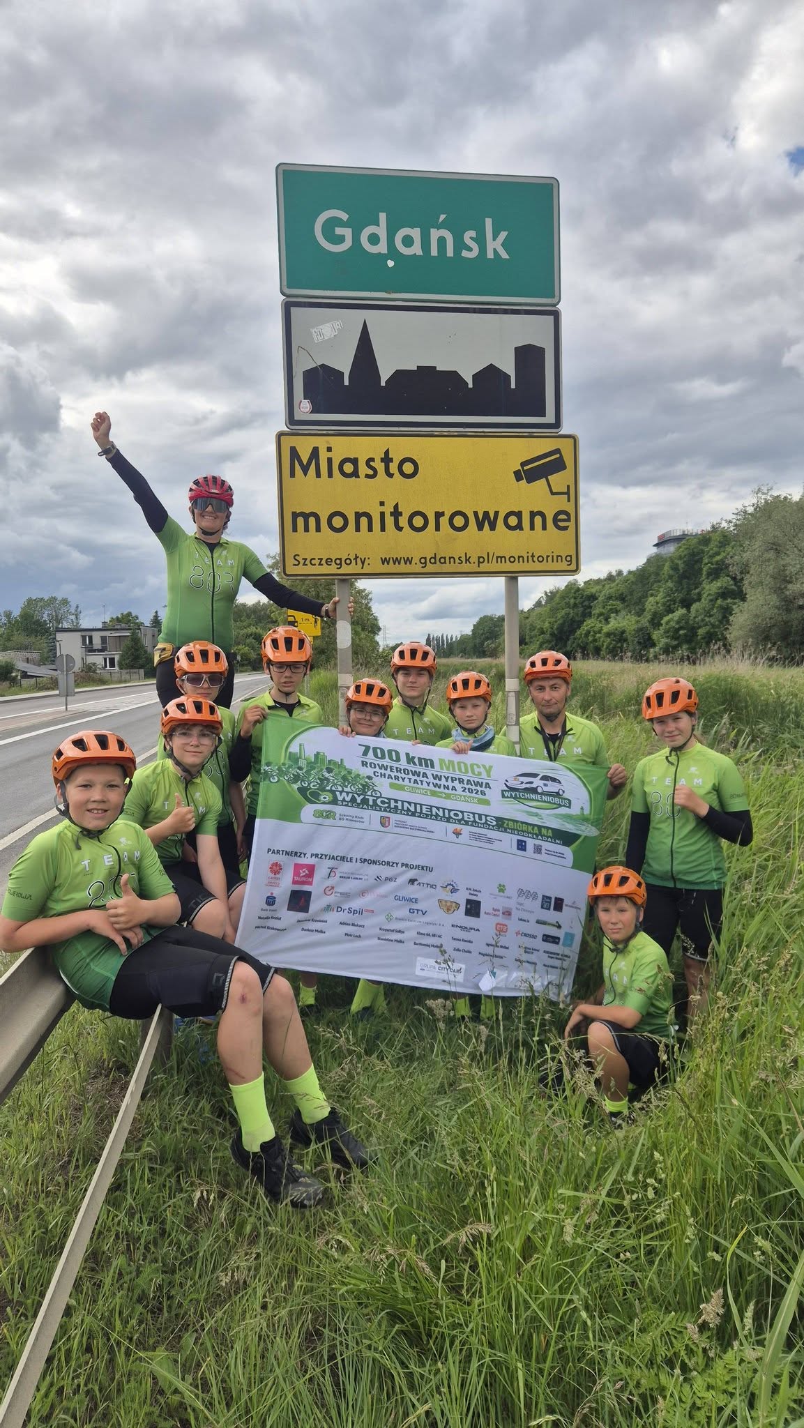 rowerzyści na tle znaku z napisem "Gdańsk"