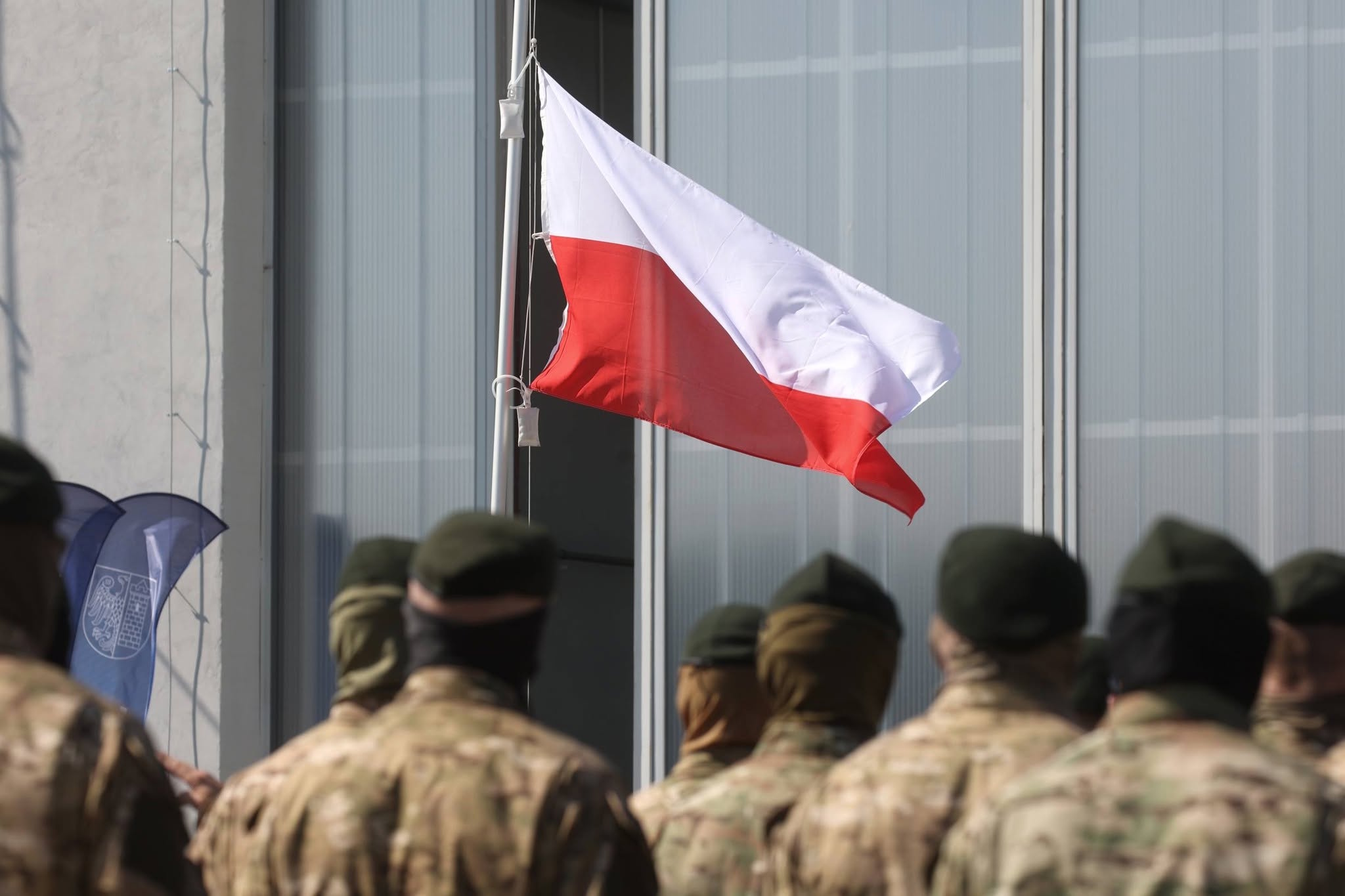 Żołnierze stojący na baczność przed flagą Polski