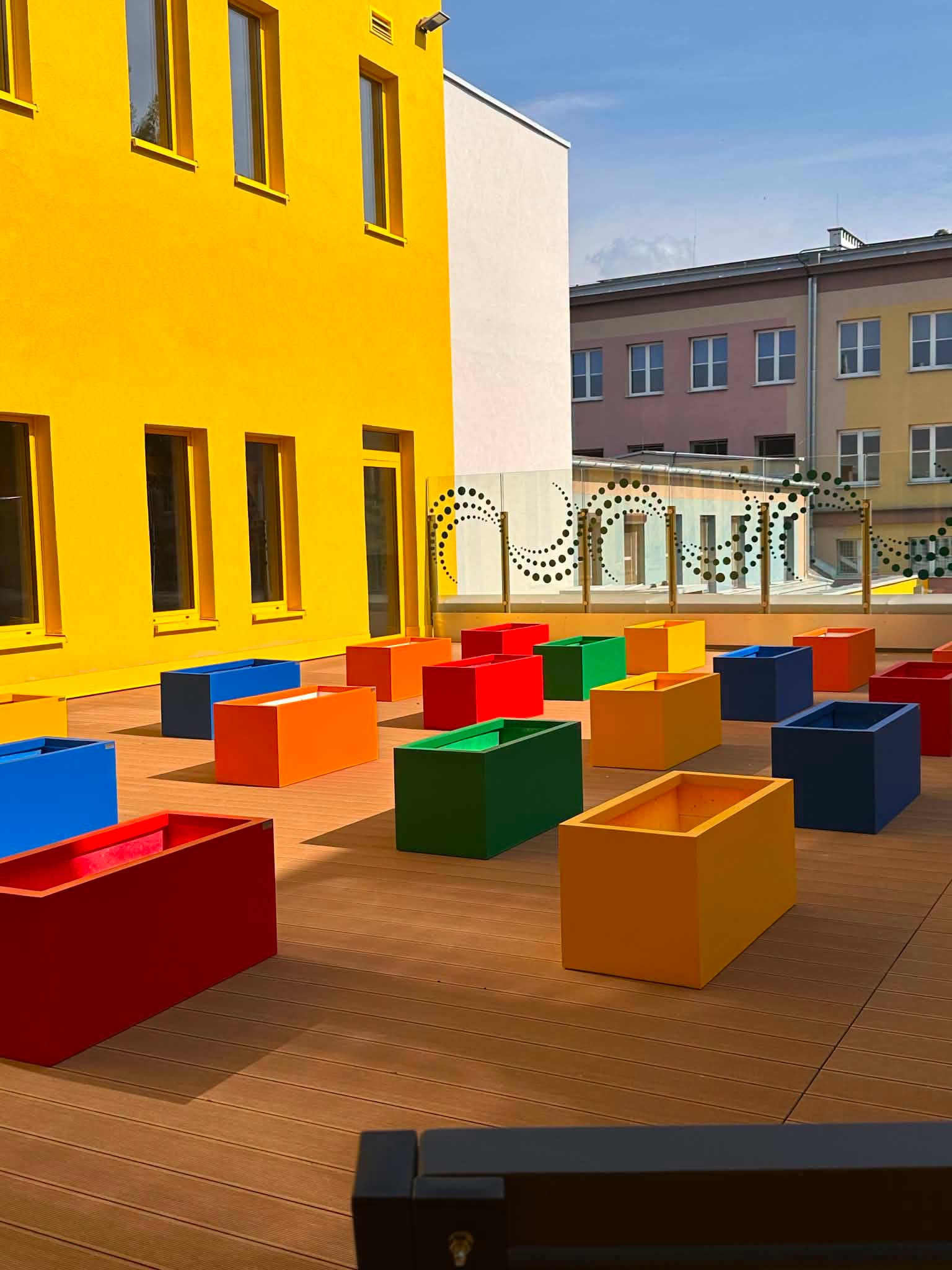 szkoła z zewnątrz z żółtą elewacją i z kolorowymi siedziskami