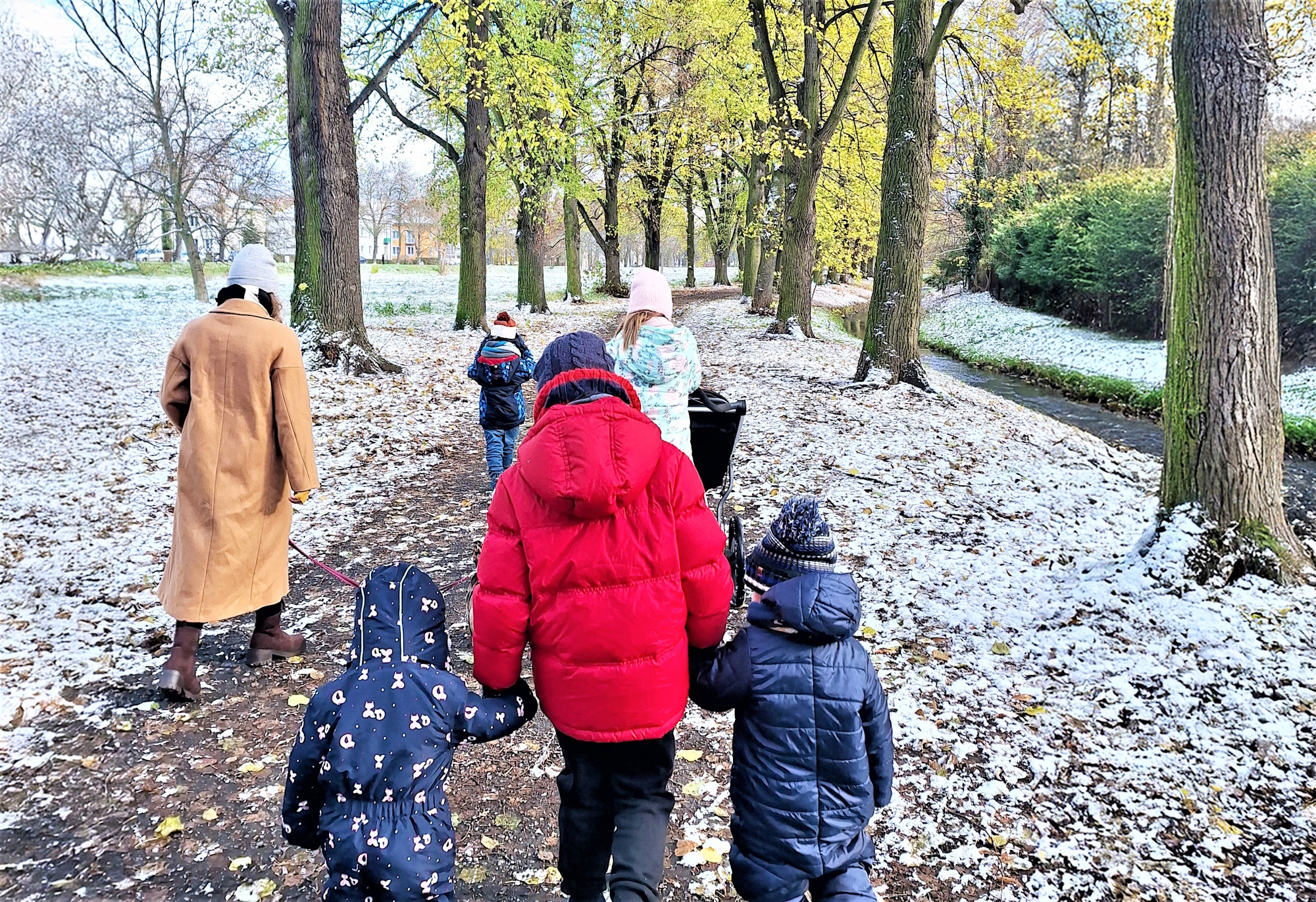 pięcioro dzieci i dorosła osoba w zimowych kurtkach na zimowym spacerze po alejce 