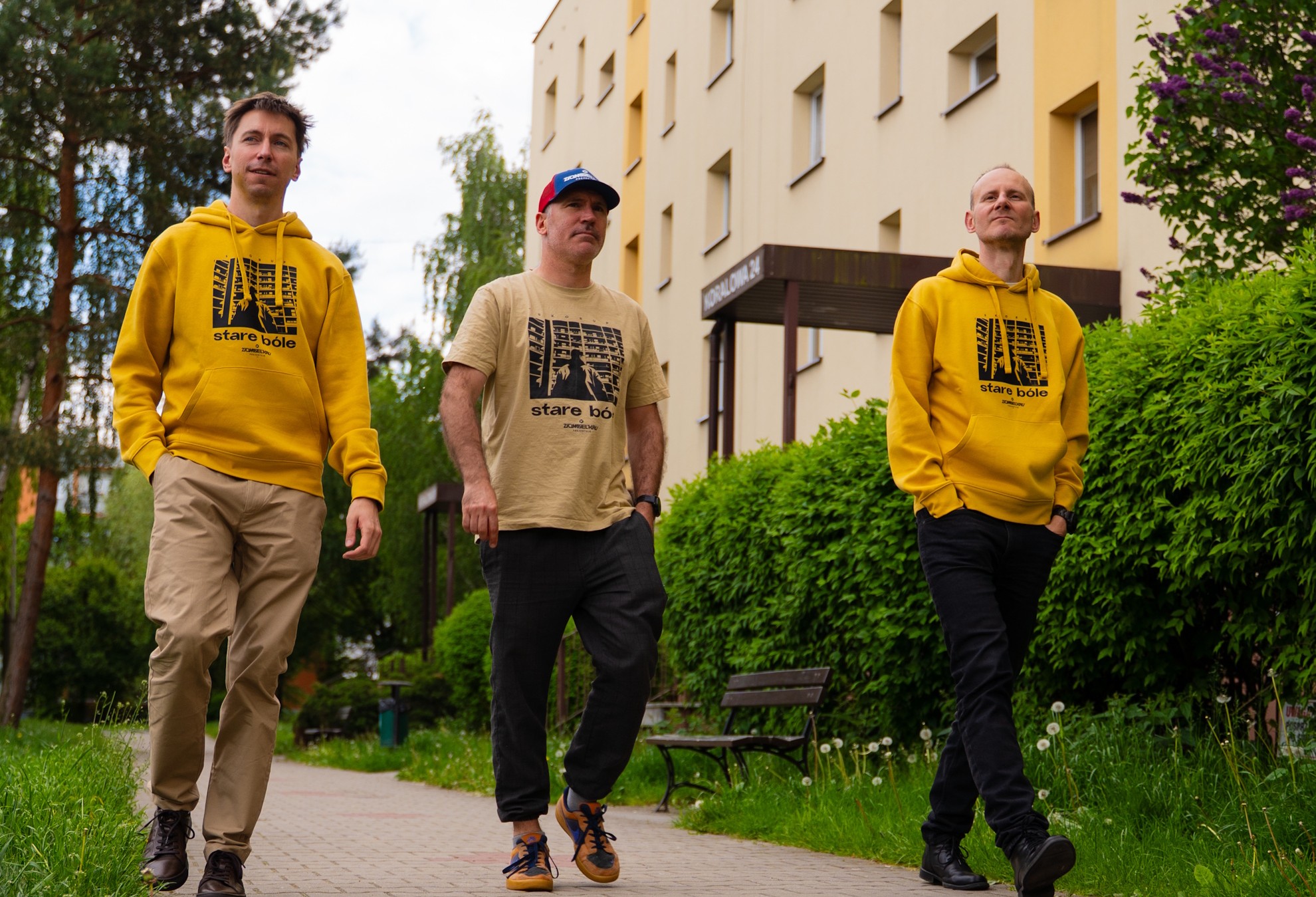 Trzech mężczyzn idzie asfalte, dwóch ma żółte bluzy